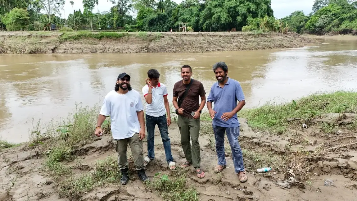 Four members of the Humrahi team standing on the scoured bank of the swollen brown river