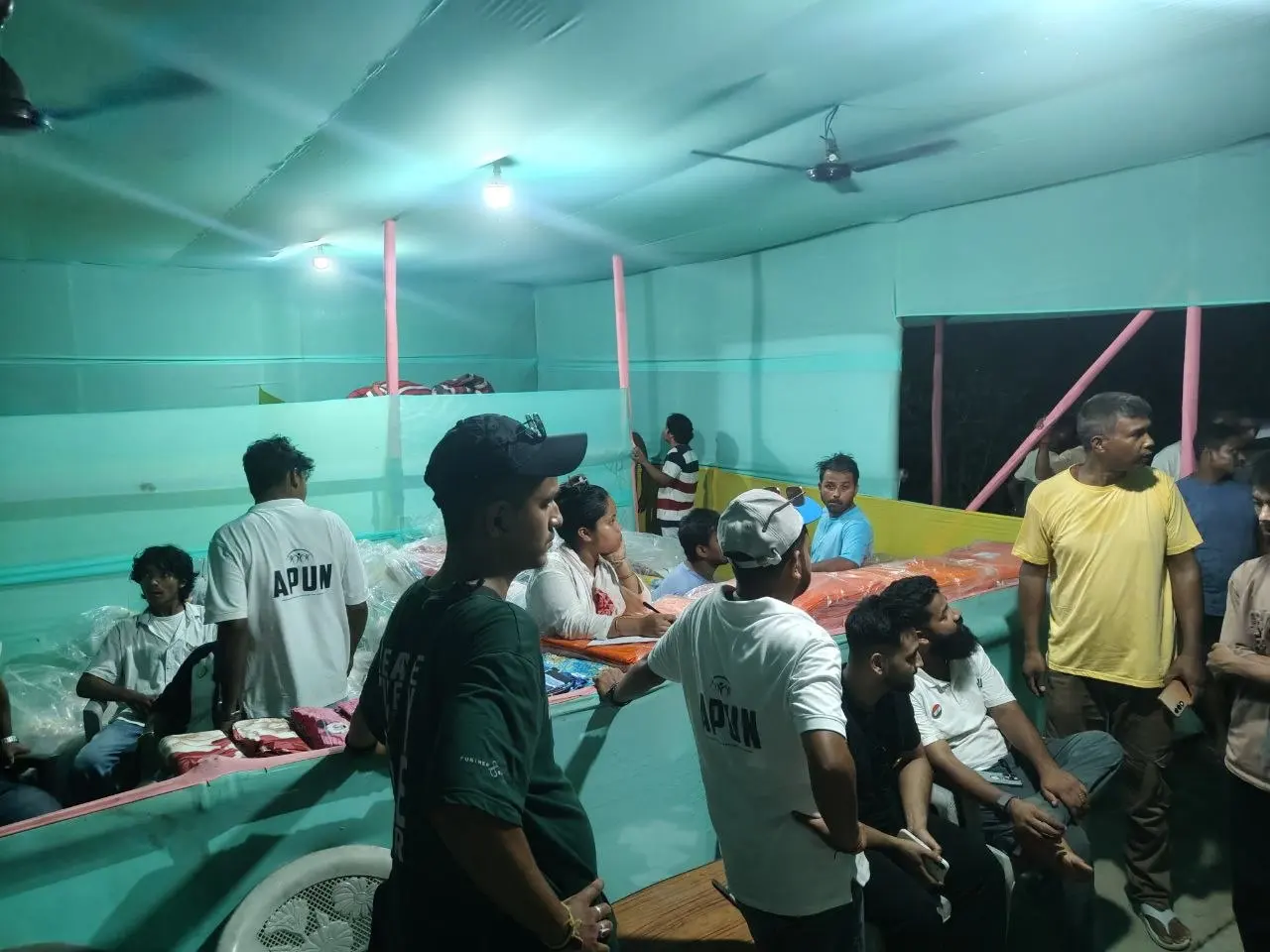 Inside the shelter hall at night as relief kits are sorted on tables and families are called forward