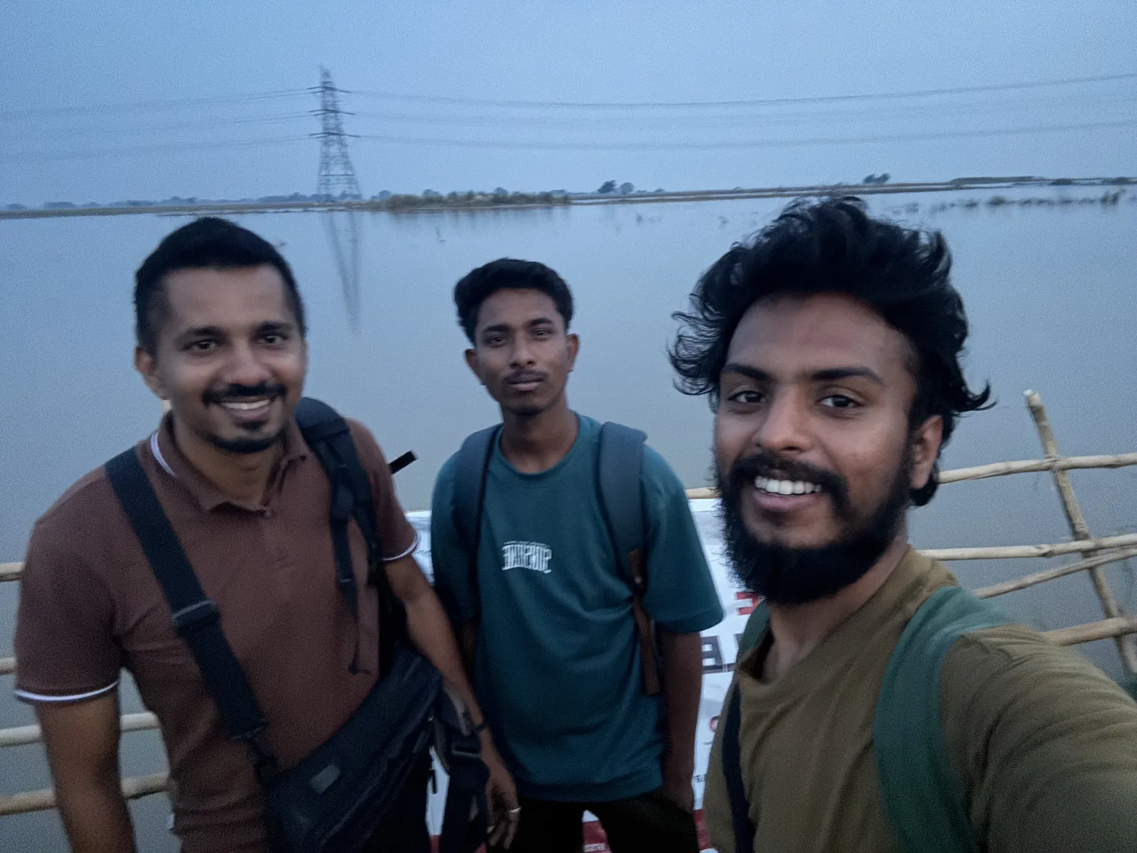 Bihar, 19 September 2026: three members of the Humrahi team in a selfie on the boat, floodwater and an electricity pylon behind them