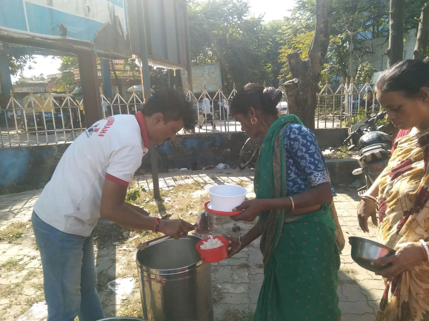 A volunteer serving a warm meal to an elderly woman in Siliguri